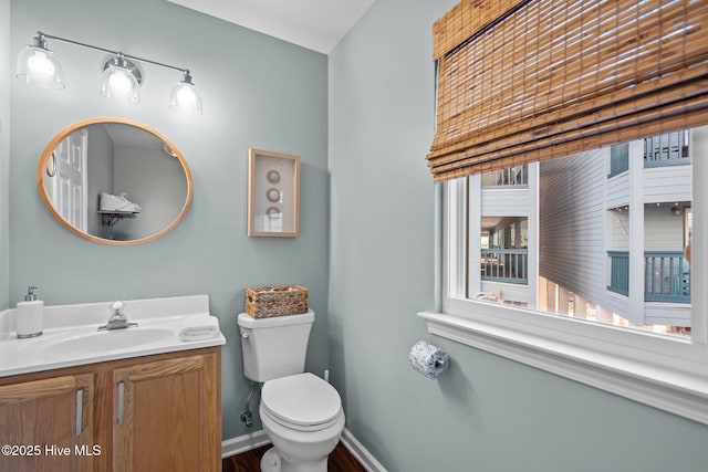 half bathroom with toilet, vanity, wood finished floors, and baseboards