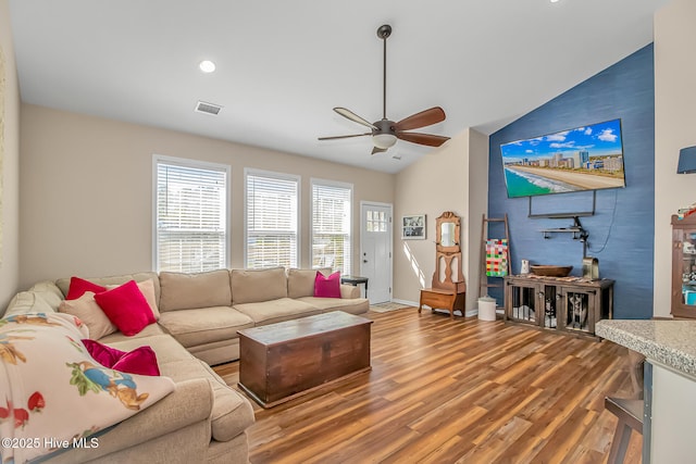 living area featuring a ceiling fan, wood finished floors, visible vents, baseboards, and lofted ceiling