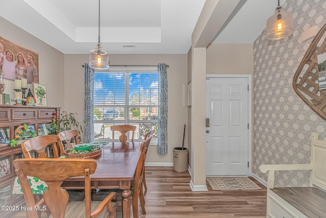 dining area with visible vents, an accent wall, baseboards, wood finished floors, and a raised ceiling