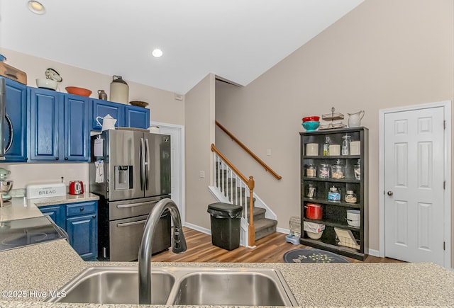 kitchen with wood finished floors, blue cabinetry, stainless steel fridge with ice dispenser, a sink, and light countertops