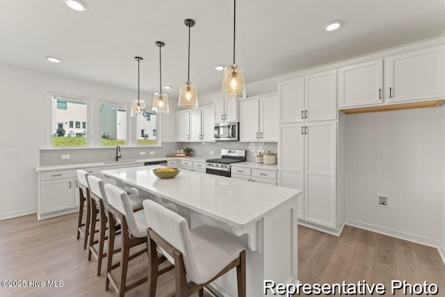 kitchen with a kitchen bar, a sink, tasteful backsplash, appliances with stainless steel finishes, and white cabinets