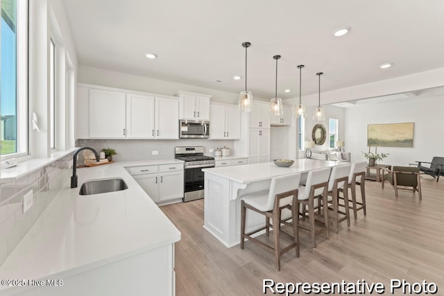 kitchen featuring a sink, white cabinets, light wood-style floors, appliances with stainless steel finishes, and a kitchen bar