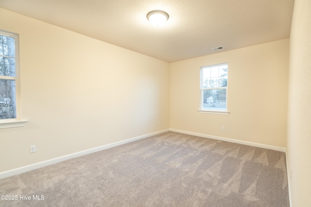 unfurnished room with carpet flooring, baseboards, visible vents, and a textured ceiling