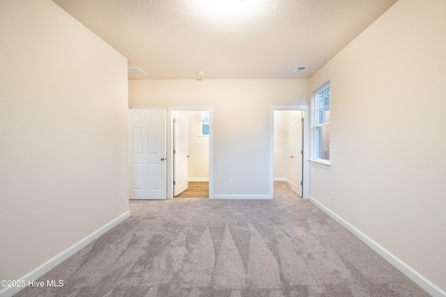 unfurnished bedroom with a spacious closet, visible vents, baseboards, carpet floors, and a textured ceiling