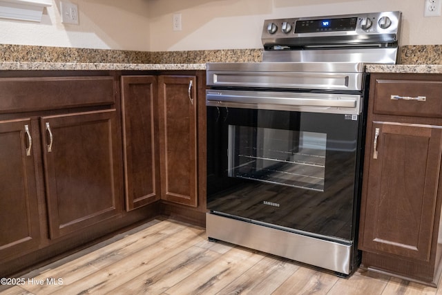 kitchen featuring stainless steel electric range oven, light stone countertops, light wood finished floors, and dark brown cabinetry