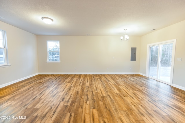 spare room with hardwood / wood-style floors, a notable chandelier, electric panel, and a textured ceiling