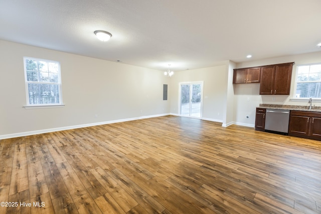 unfurnished living room with baseboards, electric panel, a sink, hardwood / wood-style flooring, and a chandelier