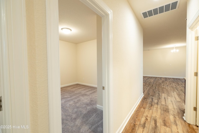 corridor featuring visible vents, baseboards, wood finished floors, and a chandelier