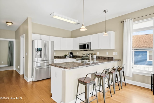 kitchen featuring dark countertops, a peninsula, stainless steel appliances, and a sink