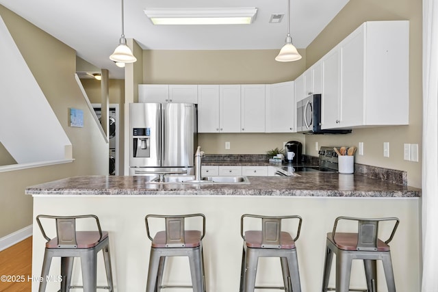 kitchen featuring appliances with stainless steel finishes, a peninsula, white cabinets, stacked washer / drying machine, and a sink