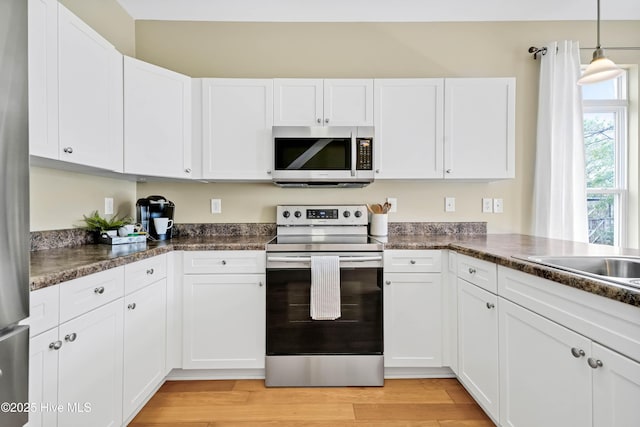 kitchen with dark countertops, white cabinetry, stainless steel appliances, and light wood-style floors