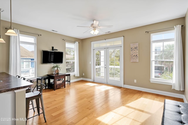 living area featuring light wood-type flooring, plenty of natural light, baseboards, and ceiling fan