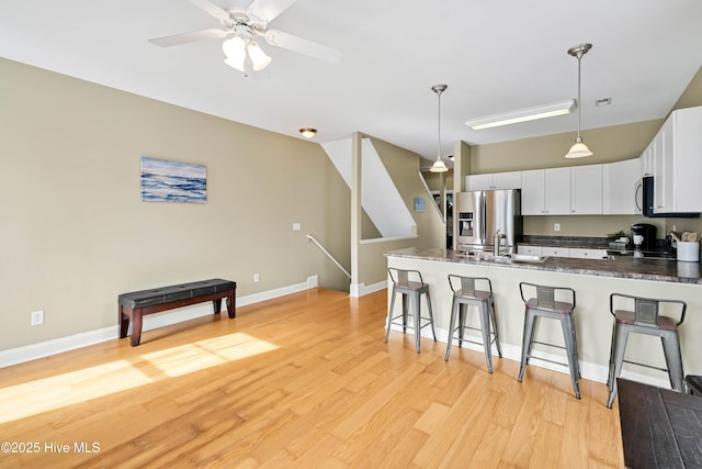 kitchen with a kitchen bar, light wood-style flooring, stainless steel appliances, a peninsula, and white cabinets