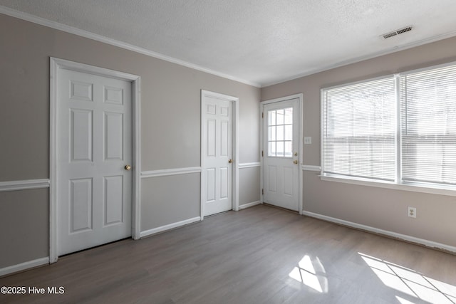 interior space with baseboards, a textured ceiling, wood finished floors, and ornamental molding