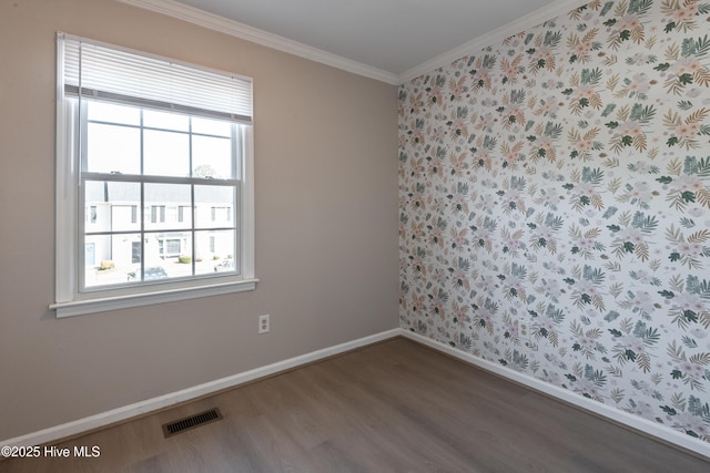 empty room featuring wood finished floors, visible vents, baseboards, and ornamental molding