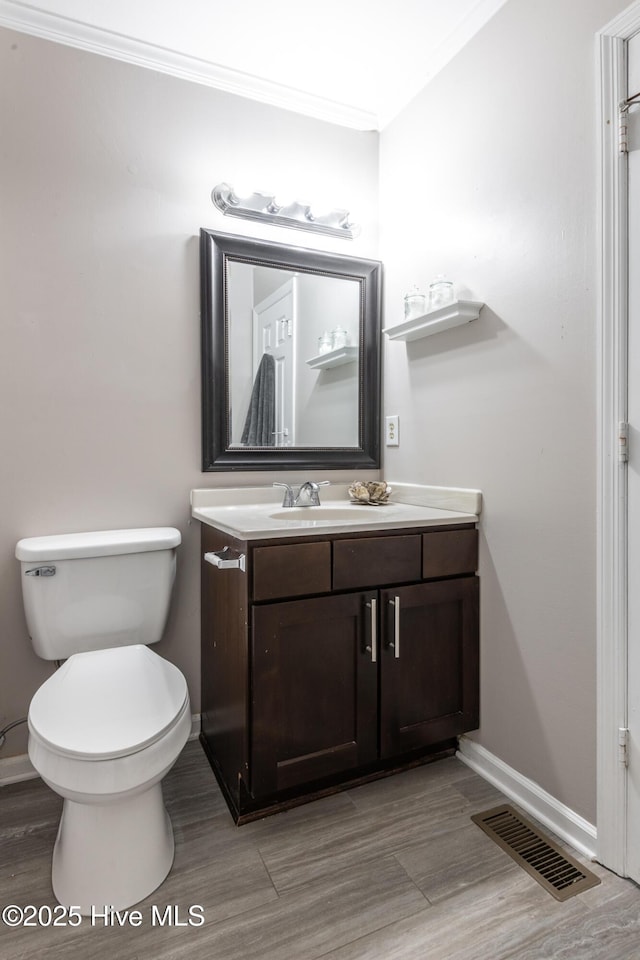 bathroom featuring vanity, baseboards, visible vents, ornamental molding, and toilet