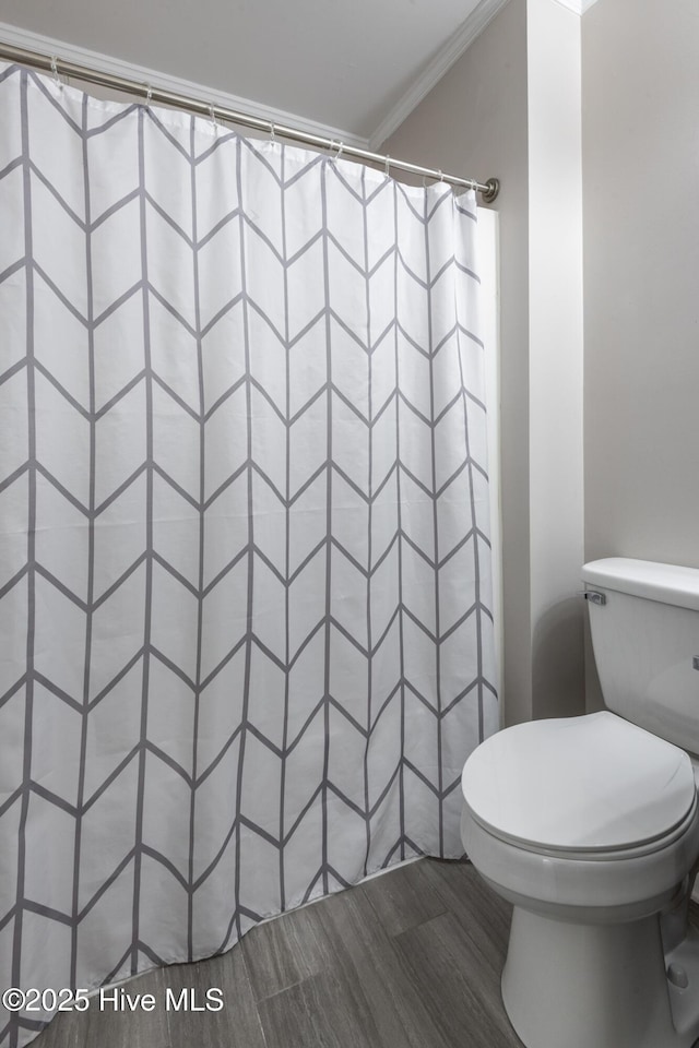 bathroom featuring a shower with shower curtain, toilet, wood finished floors, and ornamental molding