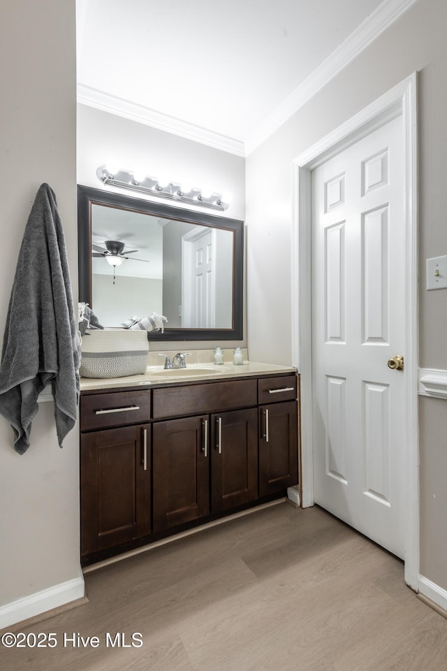 bathroom featuring vanity, wood finished floors, baseboards, and ornamental molding