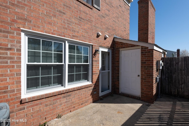 view of exterior entry with fence and brick siding