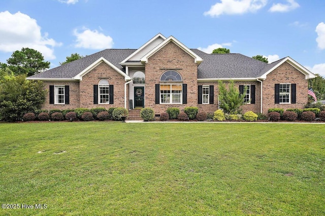 view of front of home with a front yard, brick siding, and a shingled roof