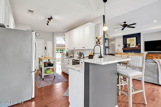 kitchen featuring hardwood / wood-style floors, visible vents, a peninsula, freestanding refrigerator, and a sink