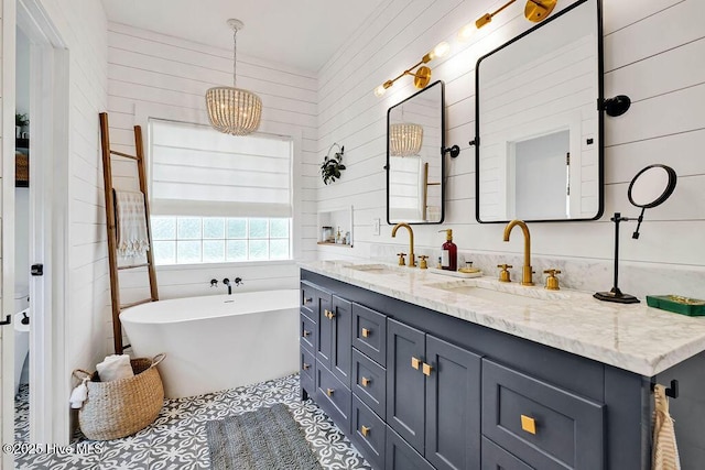 full bath featuring double vanity, a freestanding tub, a notable chandelier, and a sink