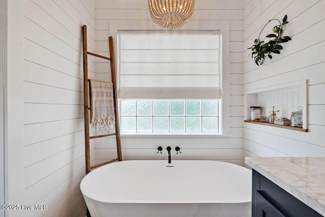 full bath with vanity, a notable chandelier, wood walls, and a freestanding bath