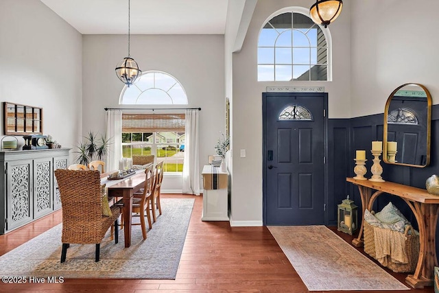 entrance foyer with a wainscoted wall, an inviting chandelier, wood finished floors, and a towering ceiling