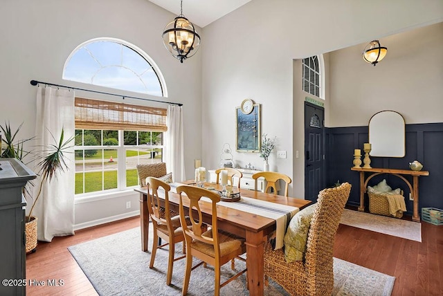 dining area featuring a chandelier, wainscoting, a towering ceiling, a decorative wall, and wood-type flooring