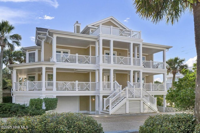 coastal inspired home featuring an attached garage, a chimney, driveway, and a balcony