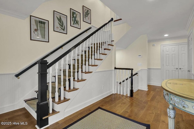 stairway with recessed lighting, a wainscoted wall, wood finished floors, and crown molding