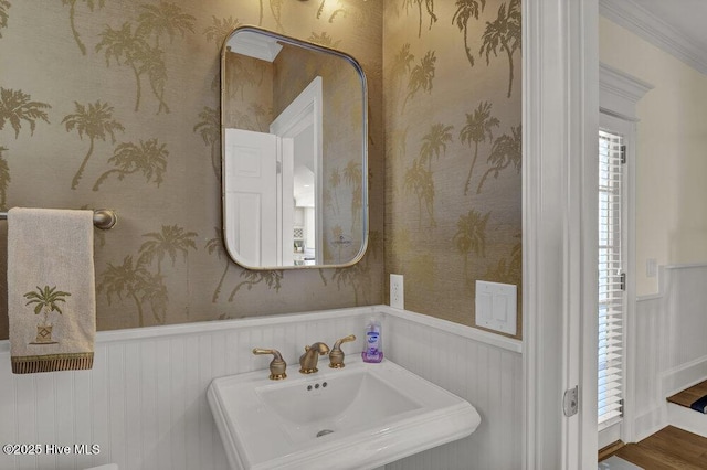 bathroom featuring wainscoting, wallpapered walls, and a sink