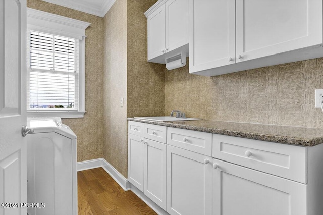 kitchen with a sink, dark wood-style floors, white cabinetry, wallpapered walls, and baseboards