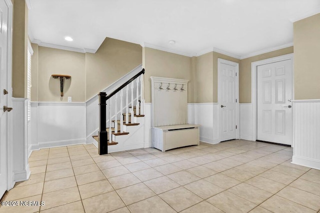 foyer entrance featuring a wainscoted wall, light tile patterned flooring, stairs, and crown molding