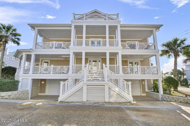 coastal home featuring stairway, a balcony, concrete driveway, and an attached garage