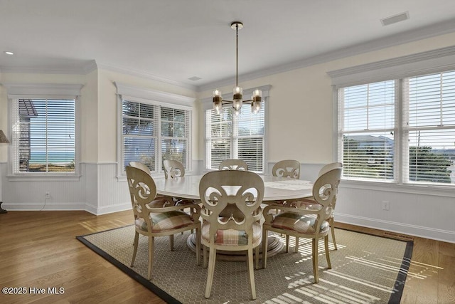 dining area with visible vents, crown molding, wainscoting, an inviting chandelier, and wood finished floors