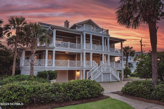 beach home with a garage, a chimney, stairs, and a balcony