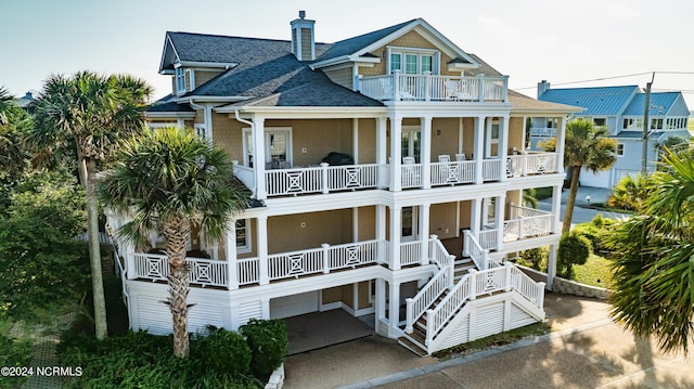 rear view of property featuring a balcony, covered porch, a chimney, and roof with shingles