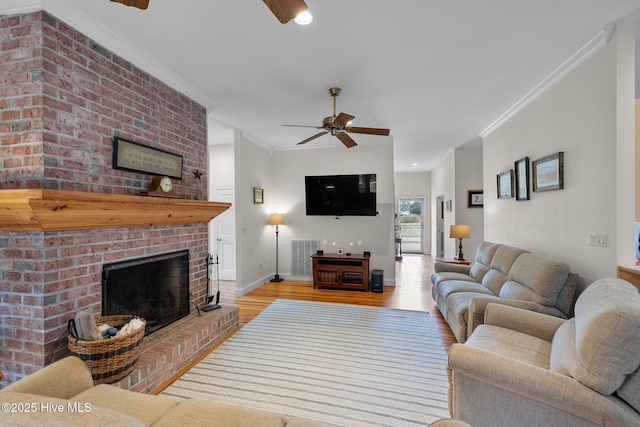 living room with crown molding, ceiling fan, visible vents, a brick fireplace, and wood finished floors