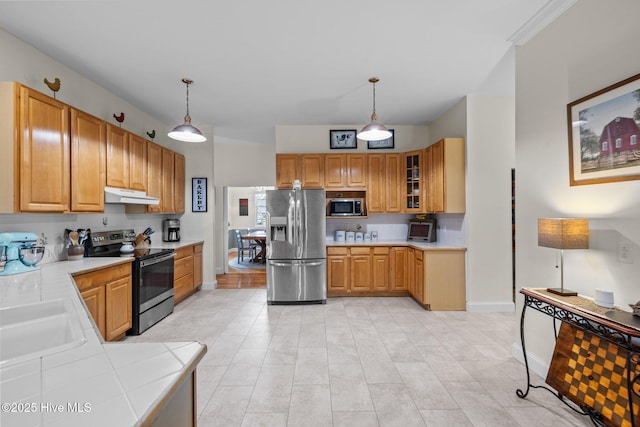 kitchen featuring a sink, stainless steel appliances, glass insert cabinets, under cabinet range hood, and decorative light fixtures