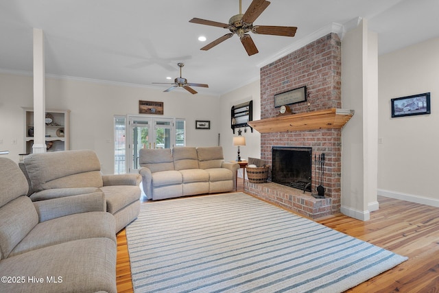 living area with wood finished floors, baseboards, ornamental molding, ceiling fan, and a brick fireplace