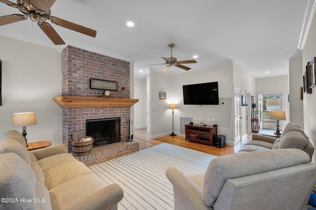 living area featuring light wood-style flooring, a ceiling fan, recessed lighting, a fireplace, and crown molding