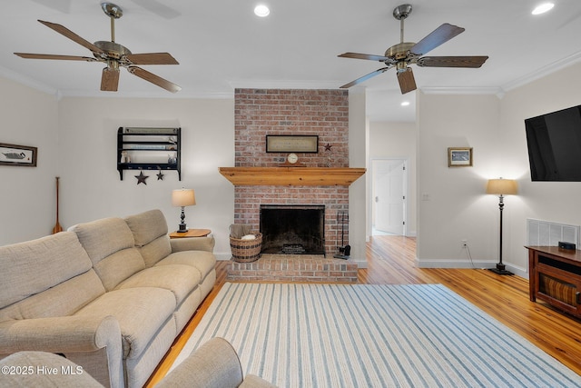 living room with light wood-style flooring, a brick fireplace, a ceiling fan, and ornamental molding