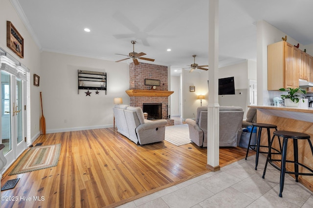 living room with visible vents, ceiling fan, crown molding, a brick fireplace, and light wood-type flooring