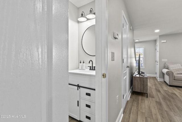 corridor featuring recessed lighting, baseboards, light wood-type flooring, and a sink