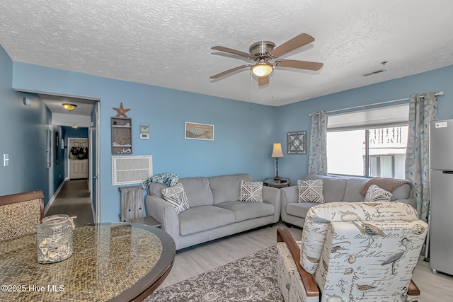 living room with ceiling fan, visible vents, a textured ceiling, and wood finished floors