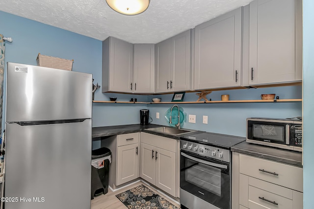 kitchen featuring a textured ceiling, dark countertops, appliances with stainless steel finishes, and a sink