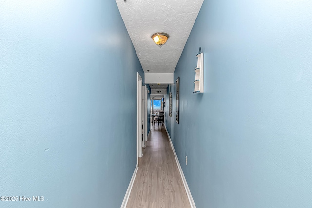 hall with wood finished floors, baseboards, and a textured ceiling