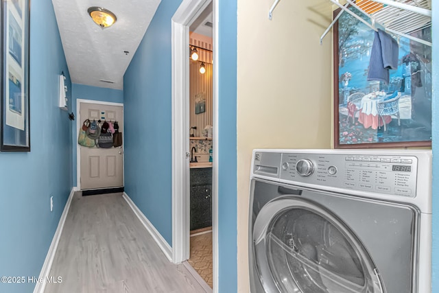 washroom featuring a textured ceiling, wood finished floors, baseboards, washer / dryer, and laundry area