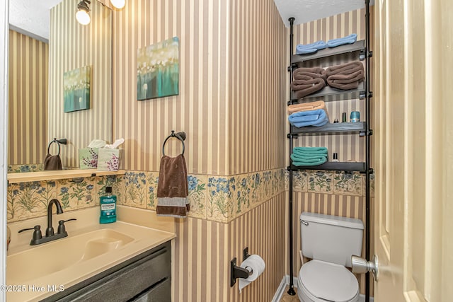 bathroom featuring a textured ceiling, toilet, vanity, and wallpapered walls